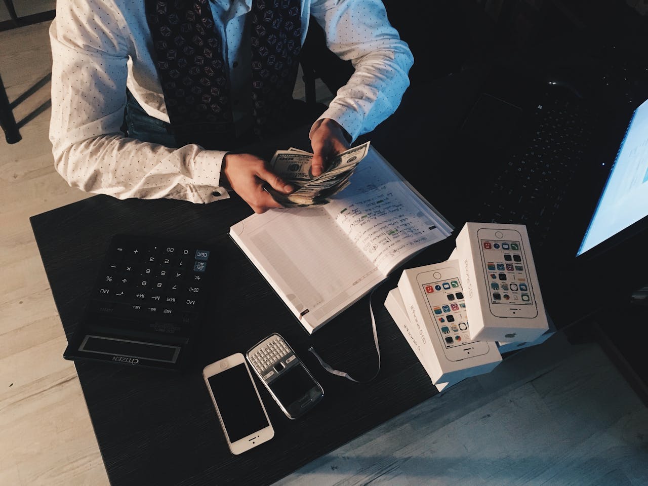 about-us-02 Businessman organizing finances with tech devices and cash on desk.